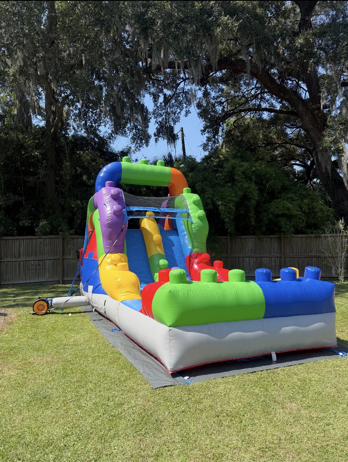 Colorful inflatable water slide set up on grass beneath oak trees in Charleston, SC